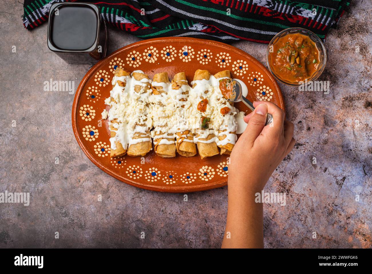 Woman's hand spooning salsa on a plate of golden potato tacos. Mexican food. Stock Photo