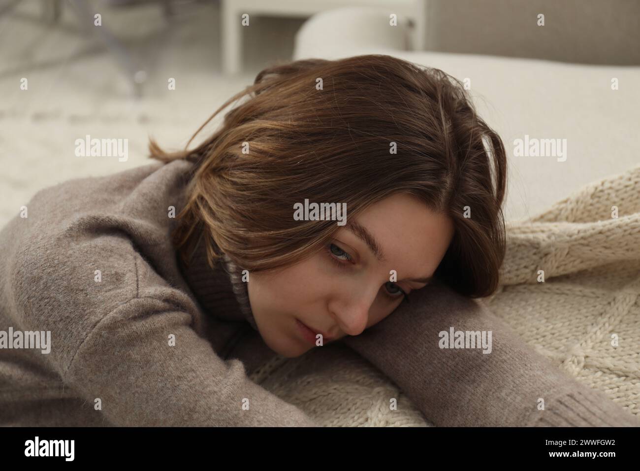 Sad young woman sitting near sofa at home Stock Photo - Alamy