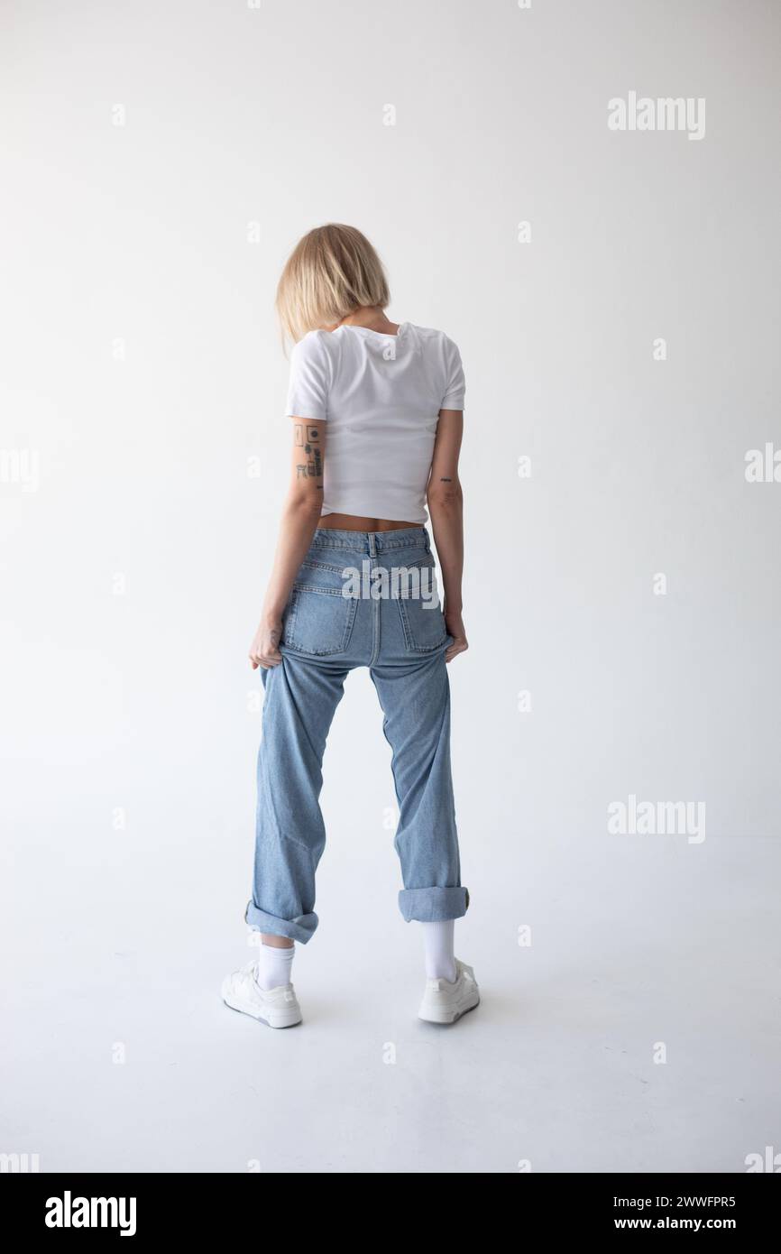 Beautiful blonde girl in a white T-shirt and blue jeans and sneakers ...