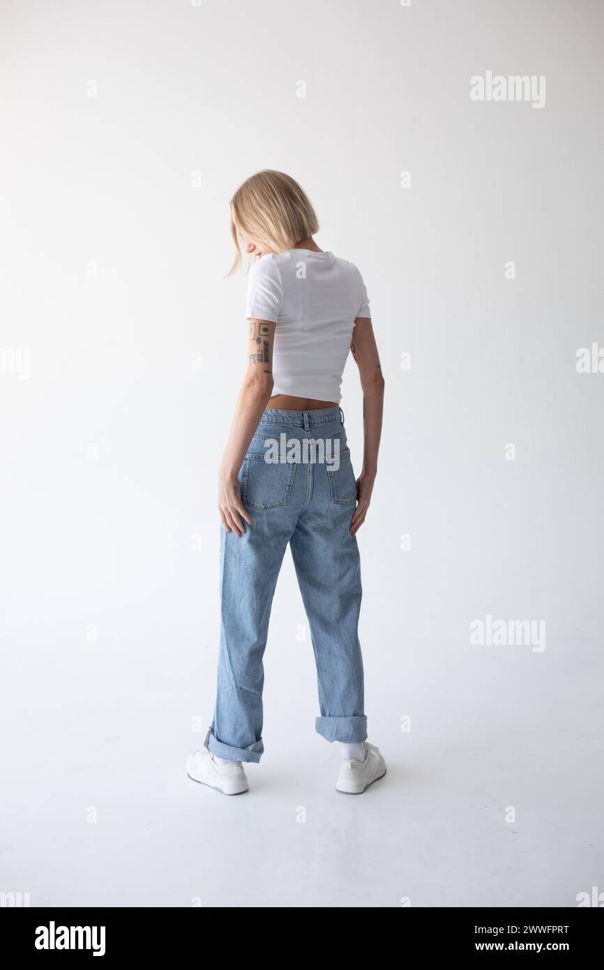 Beautiful blonde girl in a white T-shirt and blue jeans and sneakers ...