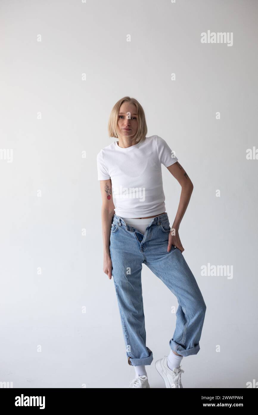 Beautiful blonde girl in a white T-shirt and blue jeans and sneakers ...