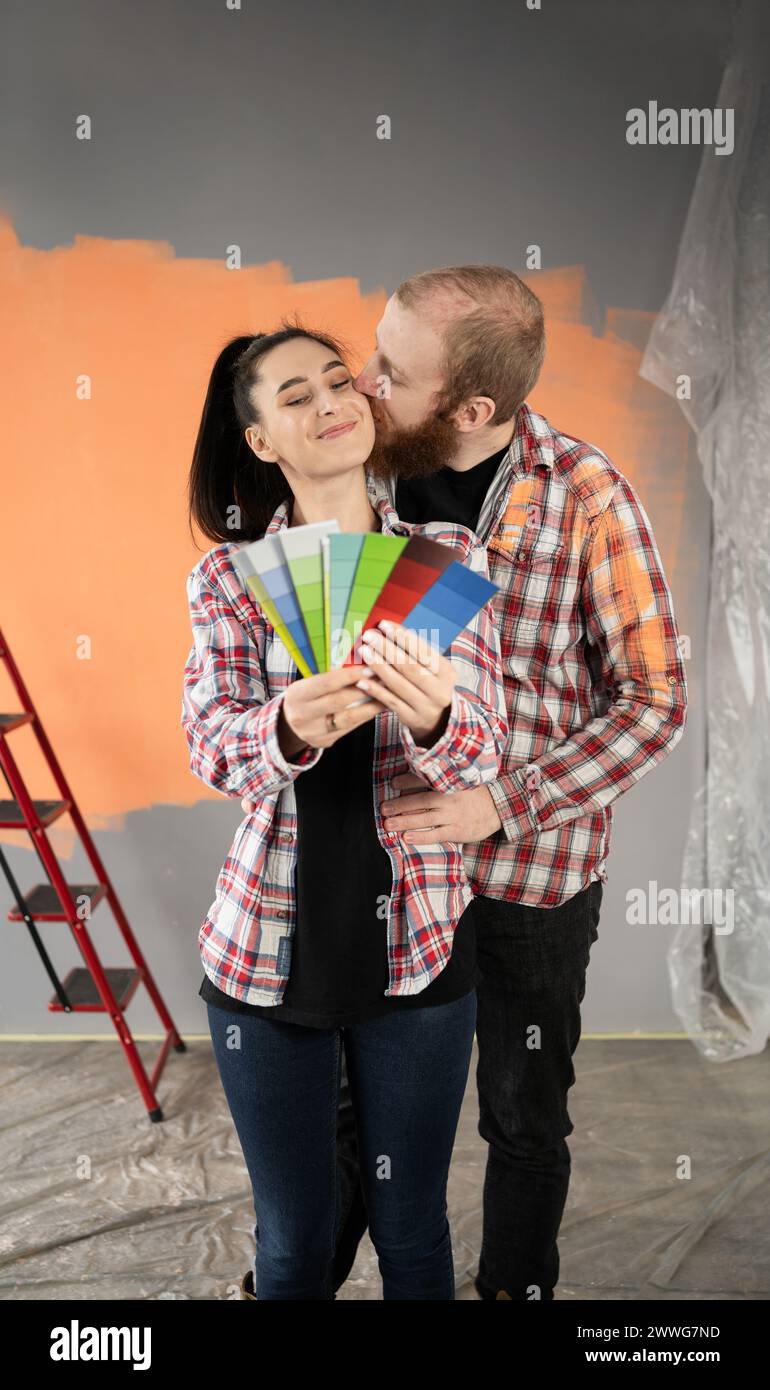 Couple of newlyweds making renovations in their new house, choosing a paint color on a palette, man kissing his wife on the cheek Stock Photo