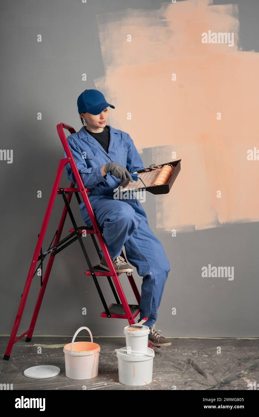 Female painter with cap and gloves painting a wall with paint roller ...