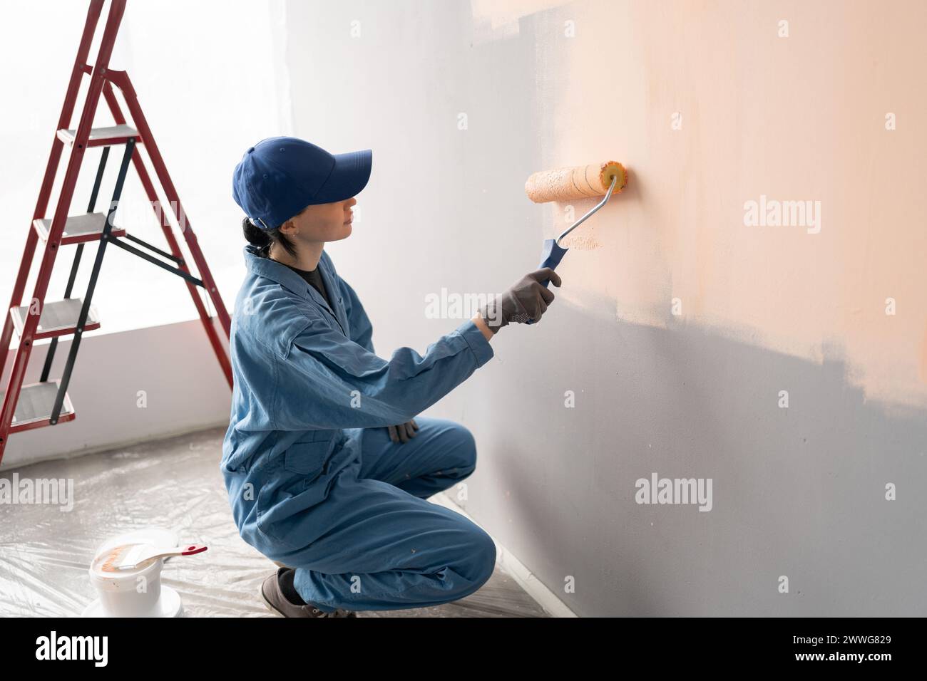 above view of female painter in overalls with cap and gloves painting a ...