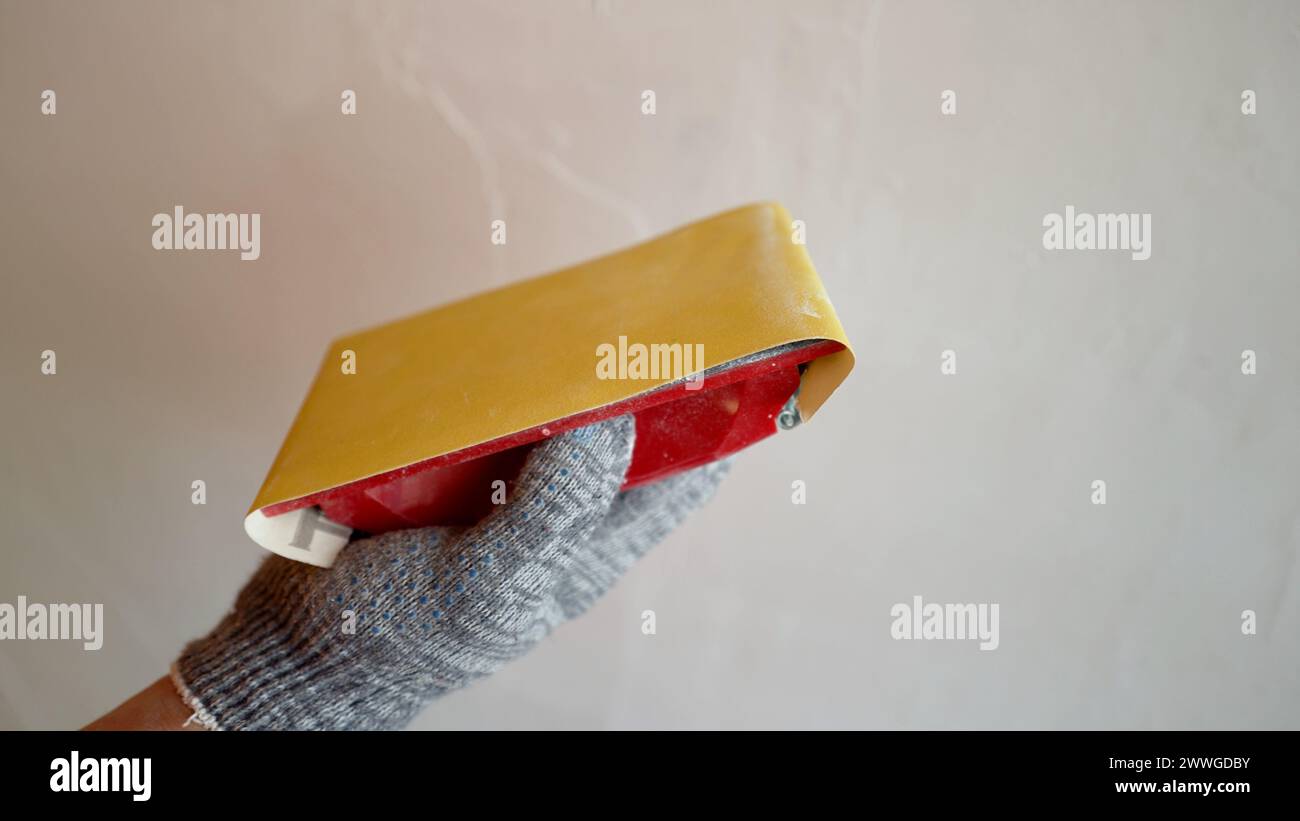 The plasterer smoothest the wall with sandpaper. Sanding walls after