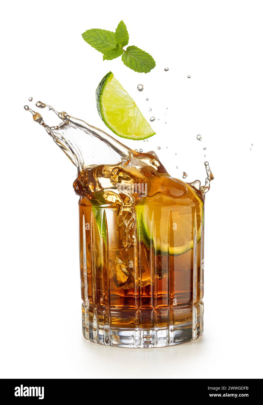 Lime wedge and mint falling into a splashing glass of rum and coke isolated on white background. Stock Photo