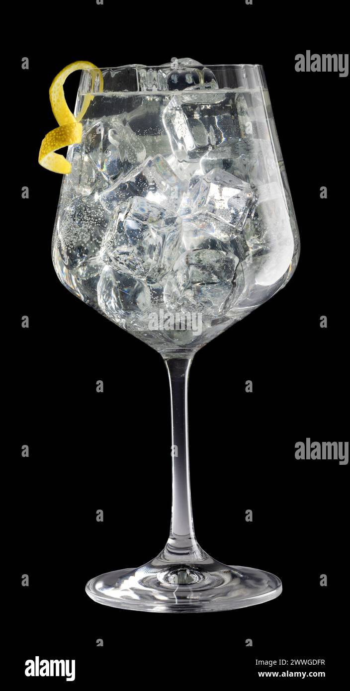 Elegant crystal glass of gin tonic garnished with spiral lemon peel isolated on black background. Stock Photo
