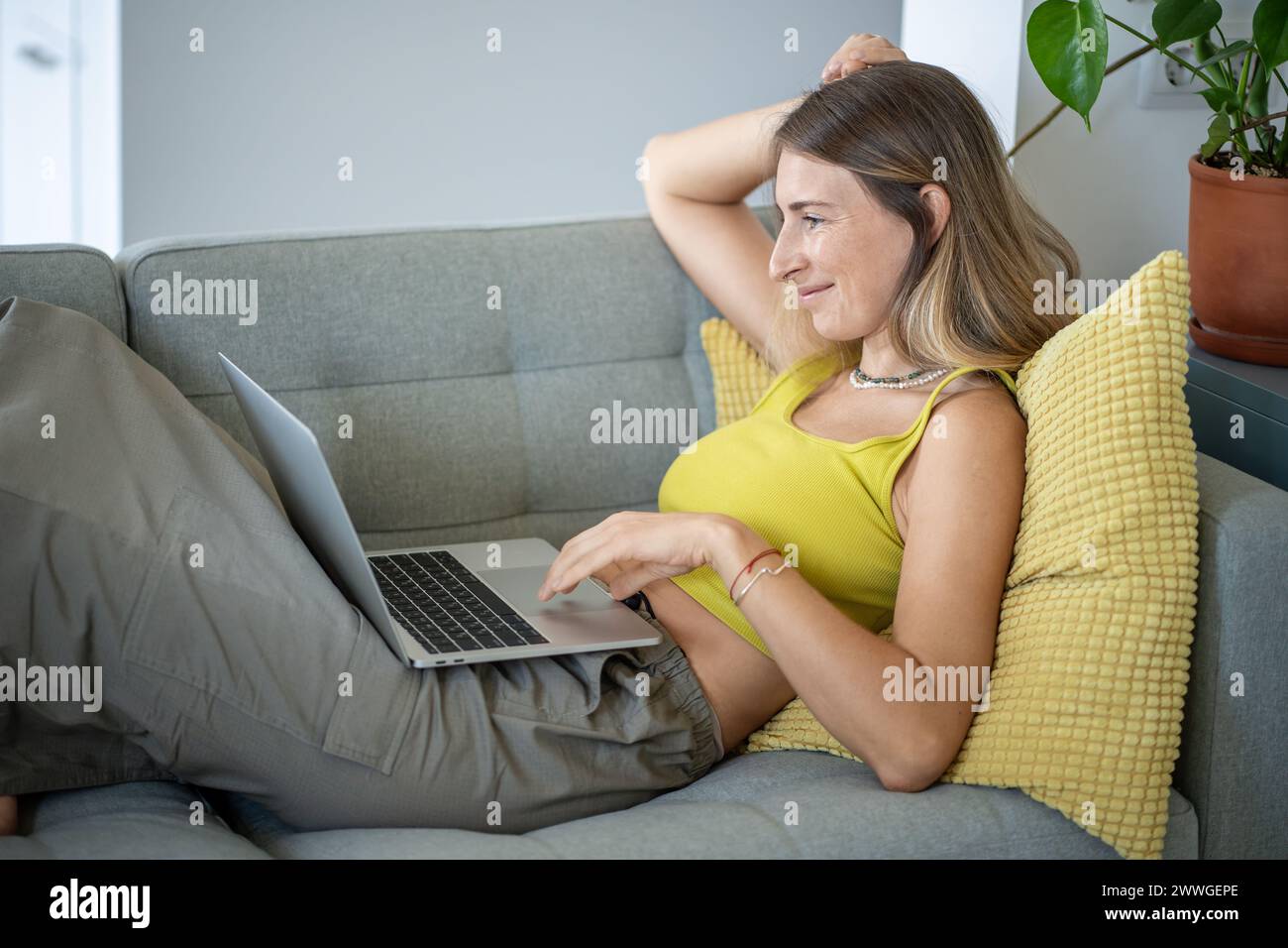 Relaxed middle aged freelancer woman online working on laptop, lying on sofa at home Stock Photo