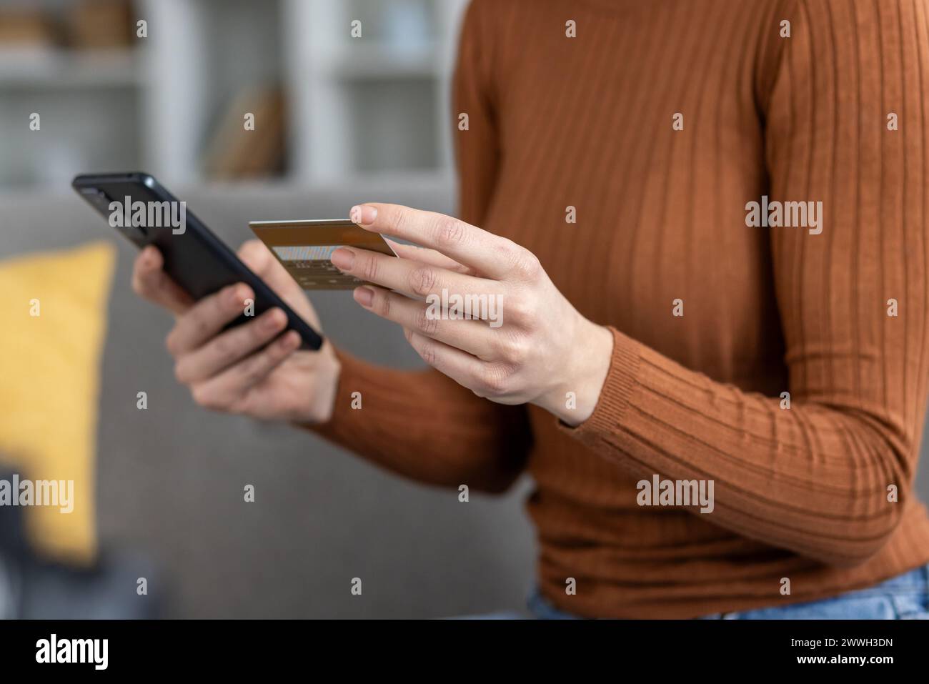 Cropped view of a person's hands holding a credit card and a smartphone, indicative of a secure online payment or mobile banking transaction. Stock Photo