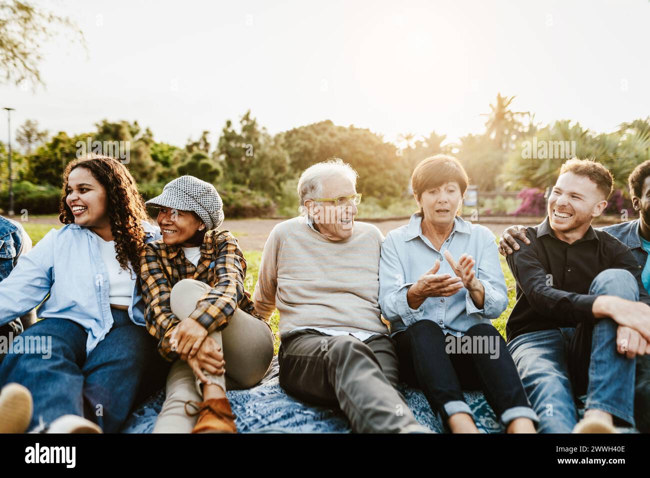 Happy multi generational people having fun sitting on grass in a public park - Diversity and friendship concept Stock Photo