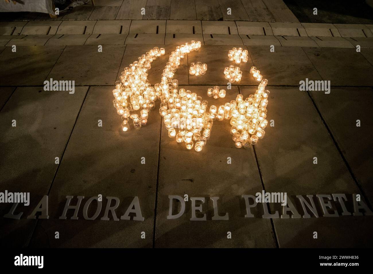 Malaga, Spain. 23rd Mar, 2024. A mosaic made with candles that depicts a panda, the symbol of WWF, is seen on the ground with slogan: 'La hora del planeta' (The hour of the earth) during the Earth Hour in the centre of Malaga. The figure made with candles is a panda, the symbol of the WWF. Thousands of cities worldwide switched off their electric lights during Earth Hour to highlight the dangers of climate change. Credit: SOPA Images Limited/Alamy Live News Stock Photo
