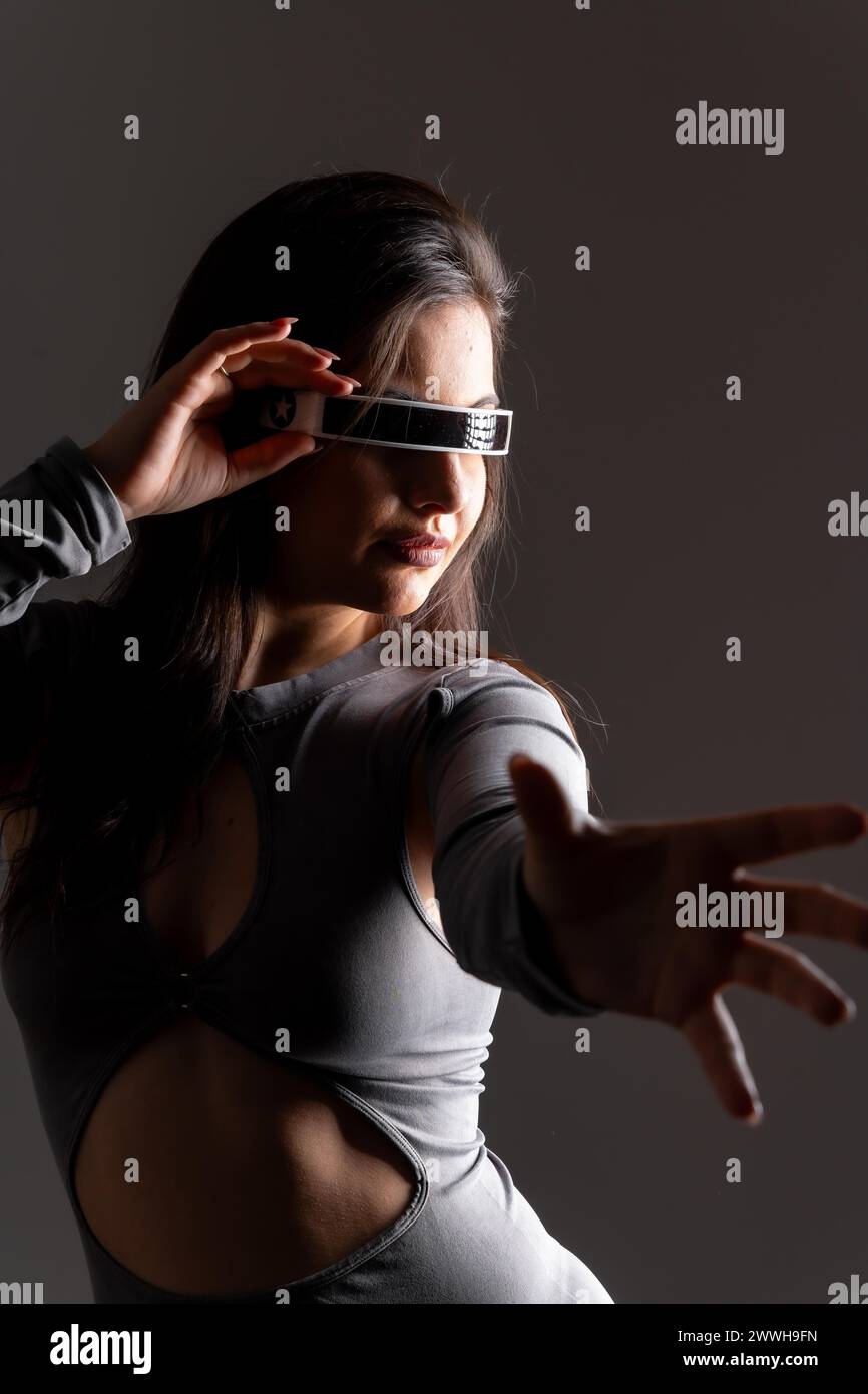 Studio portrait with grey background of a futuristic woman experiencing the metaverse world Stock Photo