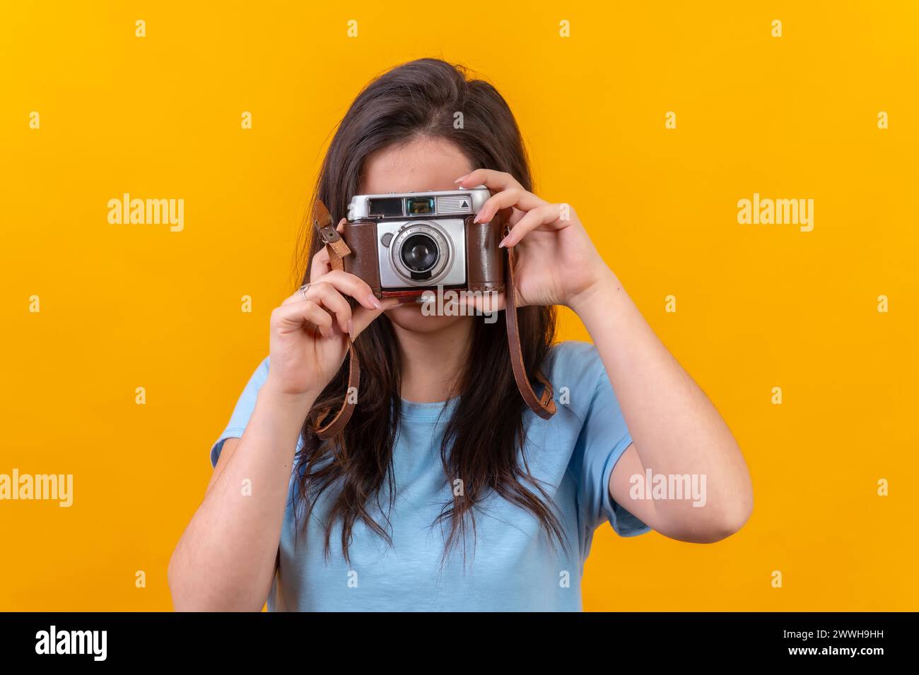 Studio portrait with yellow background of a casual young woman using a old fashioned camera Stock Photo