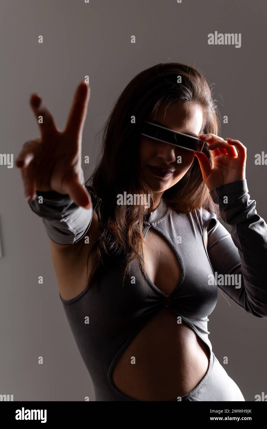 Studio portrait with grey background of a woman gesturing using futuristic artificial intelligence goggles Stock Photo