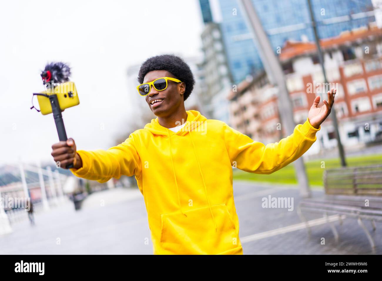 Cool african young content creator with yellow clothes streaming online in the city using mobile Stock Photo