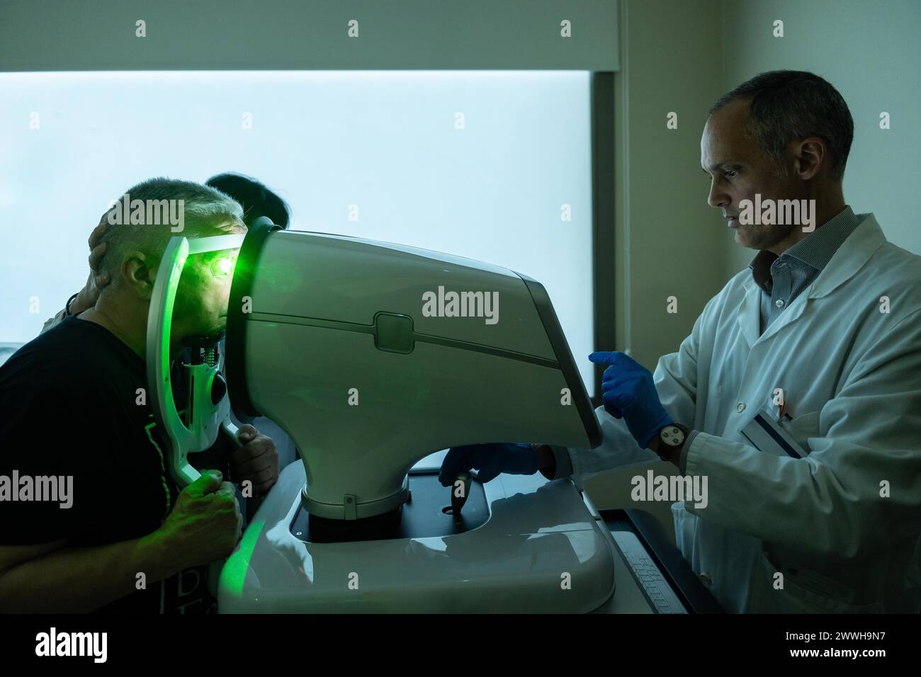 Dark photo of a clinic with ophthalmologist treating glaucoma on a senior man using laser machine Stock Photo