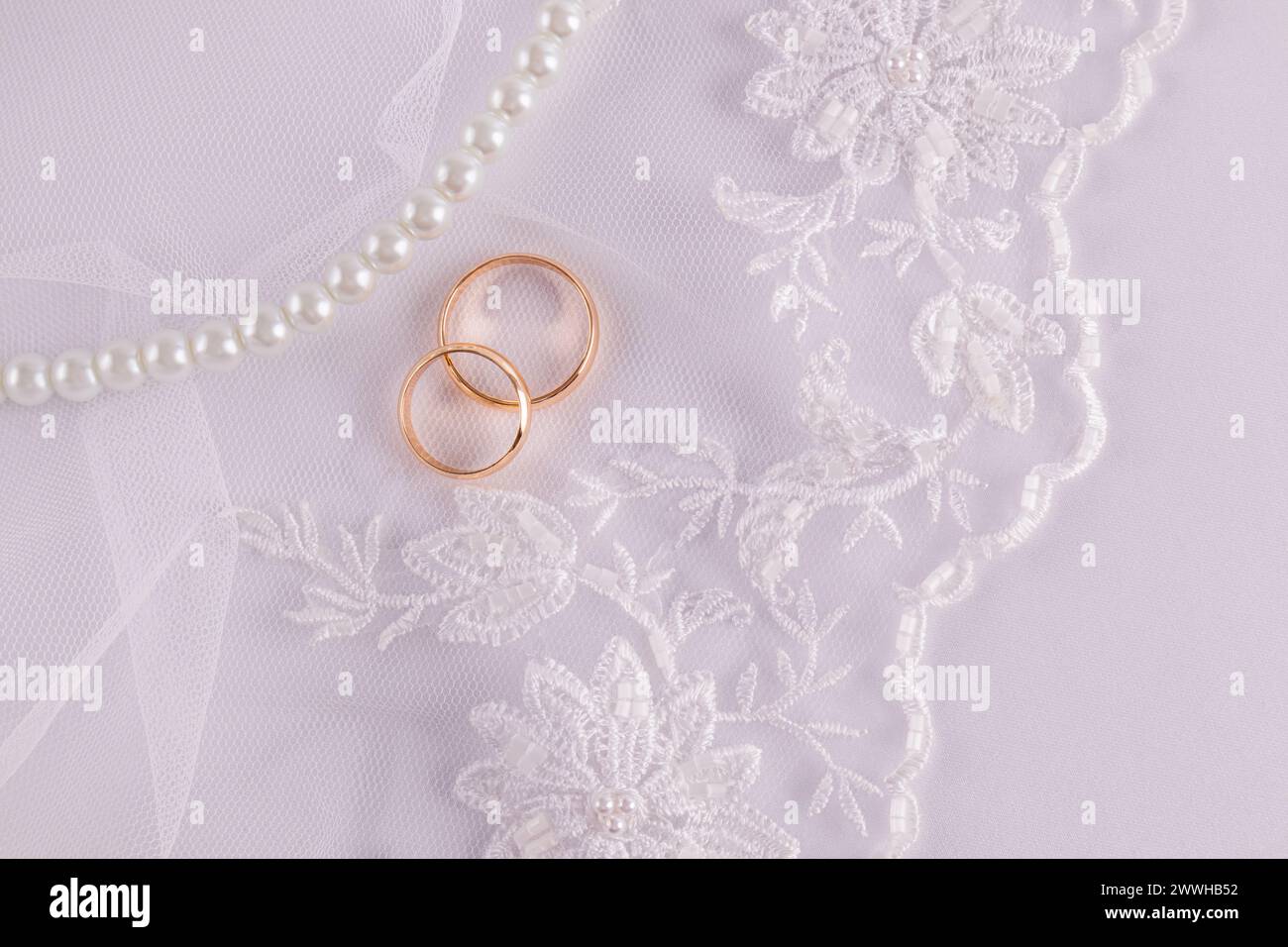 Chic wedding background for greeting card, invitation, cover design. delicate white embroidery flowers , two gold wedding rings, pearl beads Stock Photo