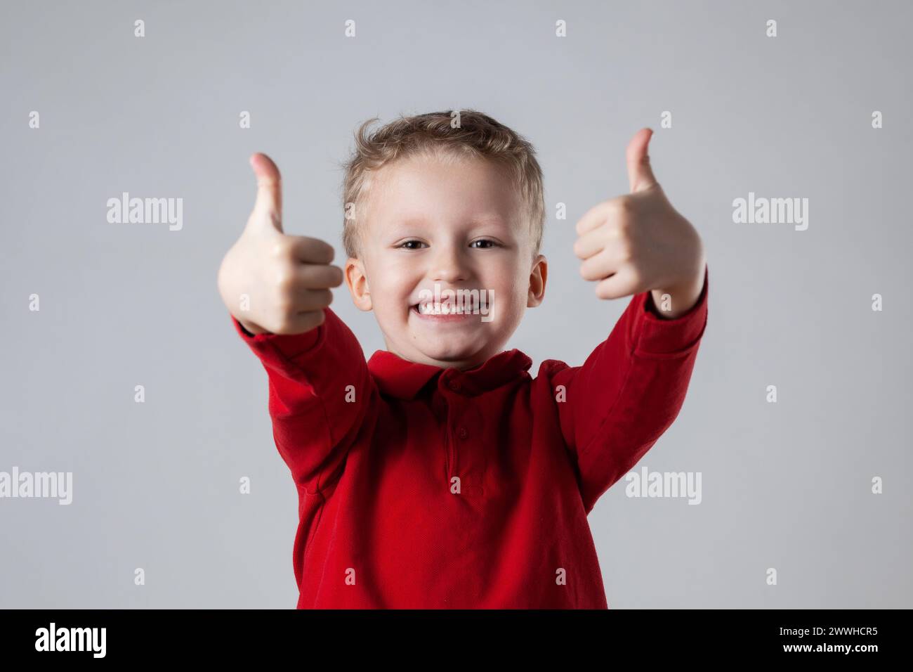 A young boy wearing a red shirt is smiling and giving a thumbs up ...