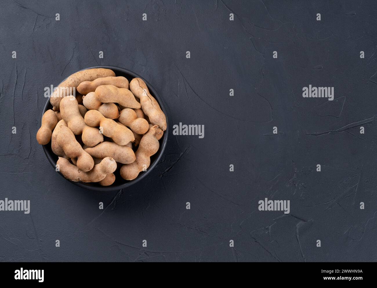 Tamarind fruit in shell and bowl on empty dark background, top view. Copy space Stock Photo