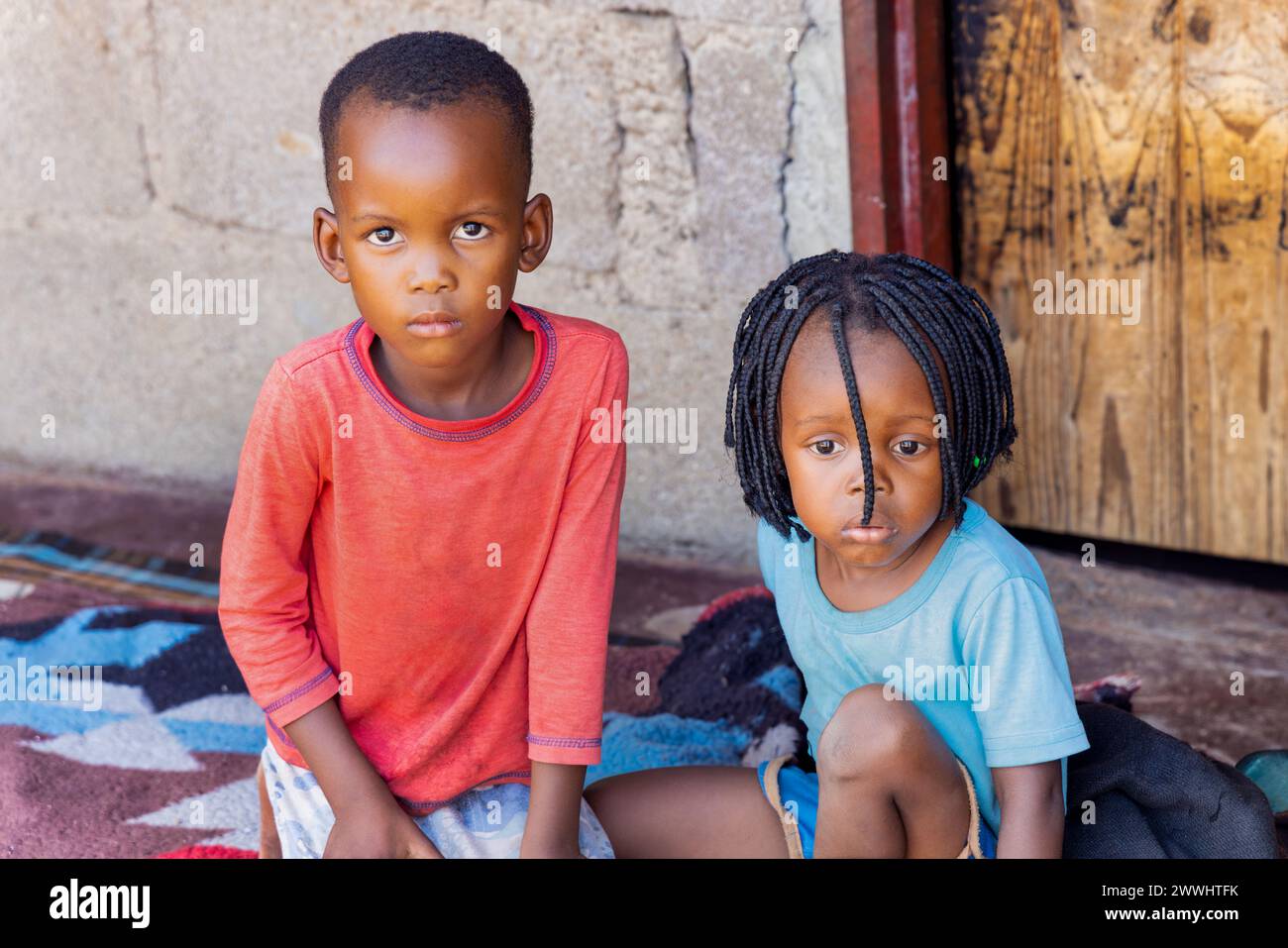 village two african kids playing on the porch in front of the house, sitting on a blanket Stock Photo