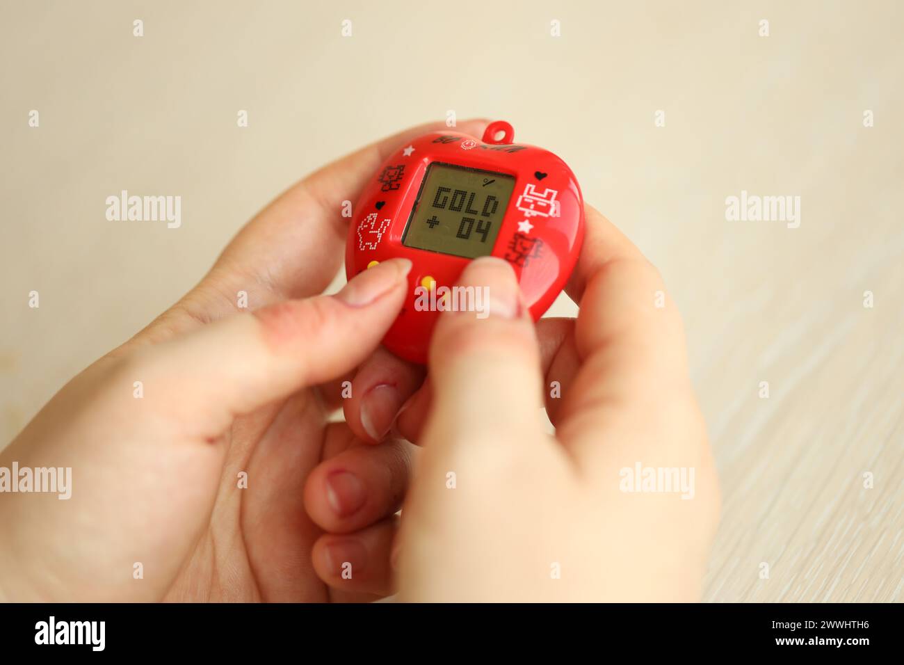 KYIV, UKRAINE - MARCH 9, 2024 Retro pet keychain game tamagotchi in red plastic case in female hands close up Stock Photo