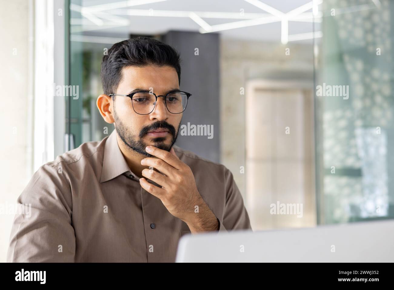 Young Indian businessman in a serious thinking pose, working on his laptop at an office, showing dedication and focus. Stock Photo