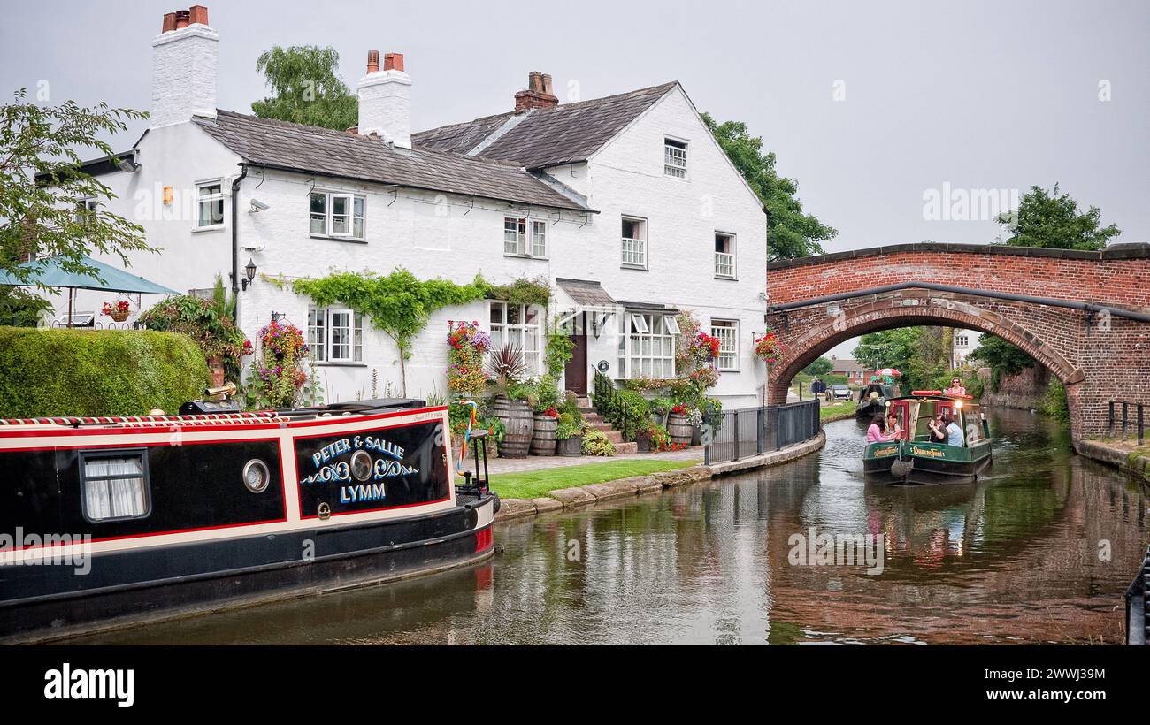 Day hire boat cruising through the arched canal bridge with moored boat outside house on the Bridgewater Canal,  England, UK, Britain, Lymm, Cheshire Stock Photo