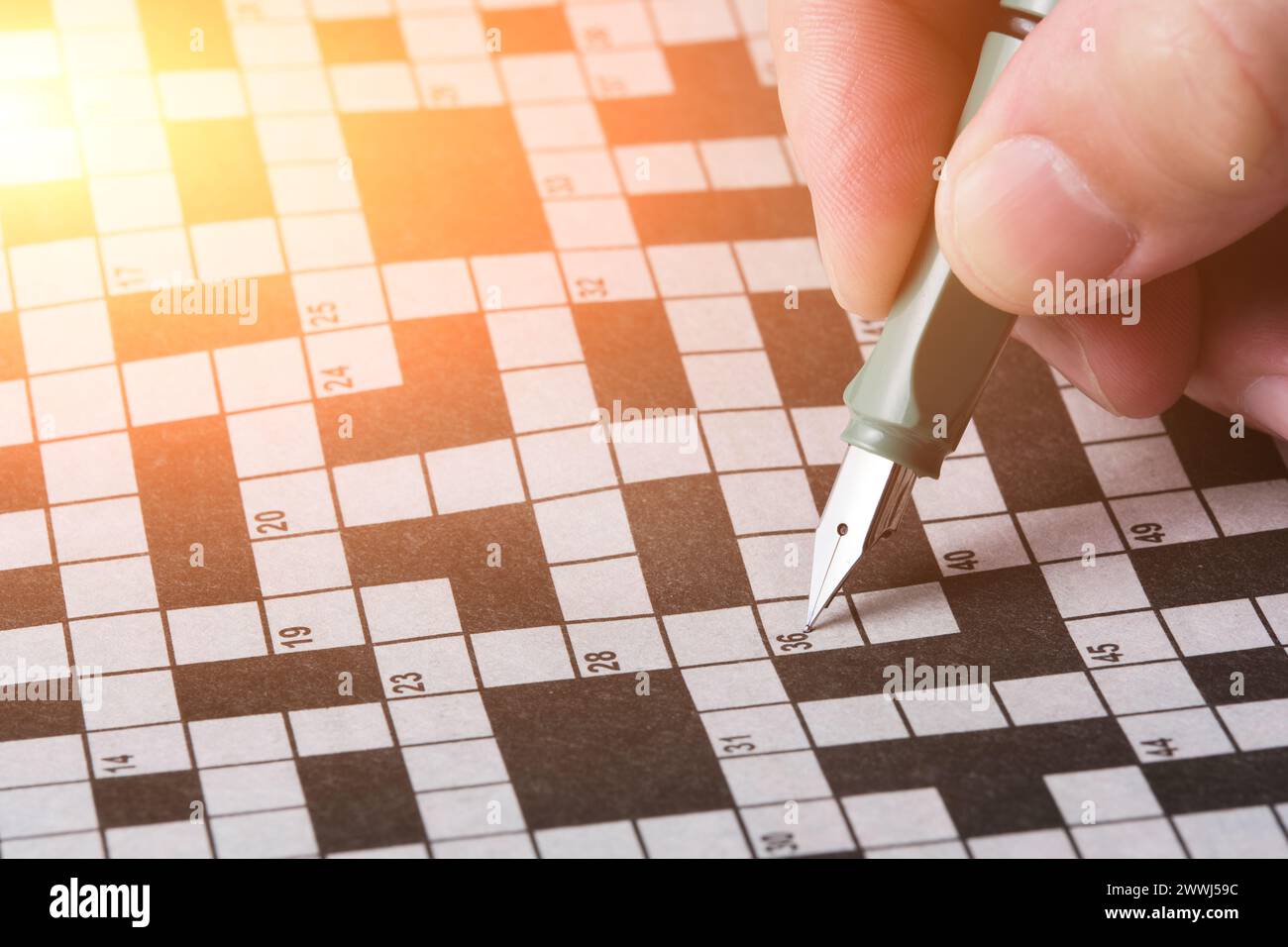 Hand with a fountain pen on the background crossword puzzle sheet Hand with a fountain pen on the background crossword puzzle sheet