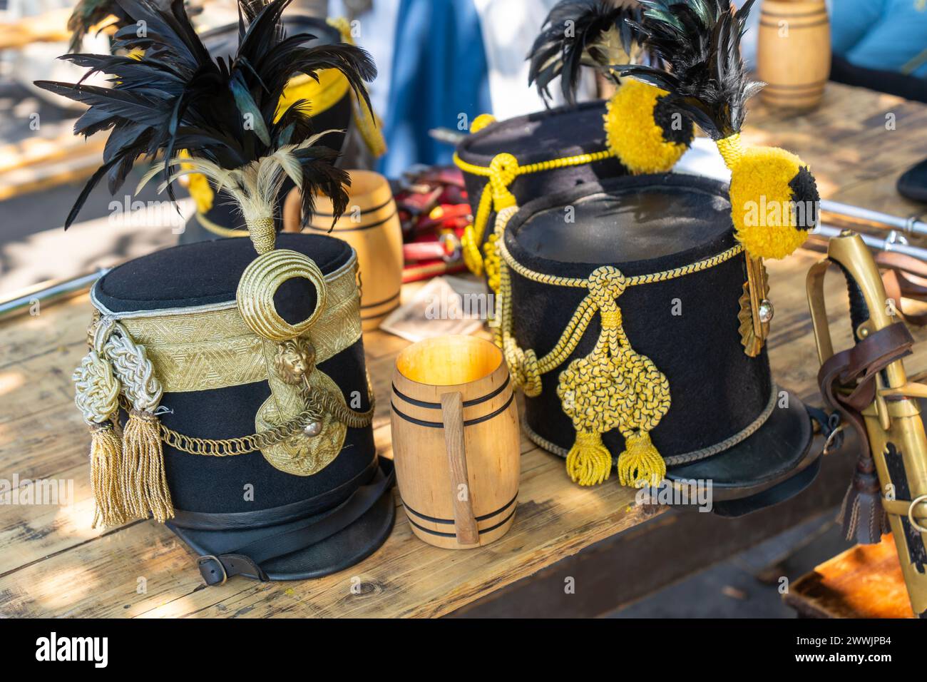 Hussar hats with black and yellow trim on an outdoor pub table full of wooden cups Stock Photo