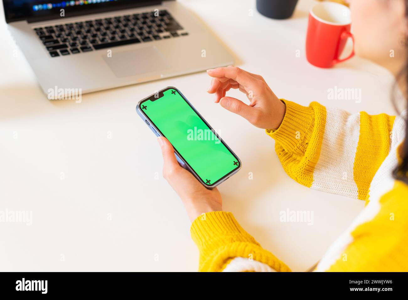 Close-up unrecognizable woman in a sweater working in using a blank modern smartphone with a green screen in chroma key display sitting table office Stock Photo