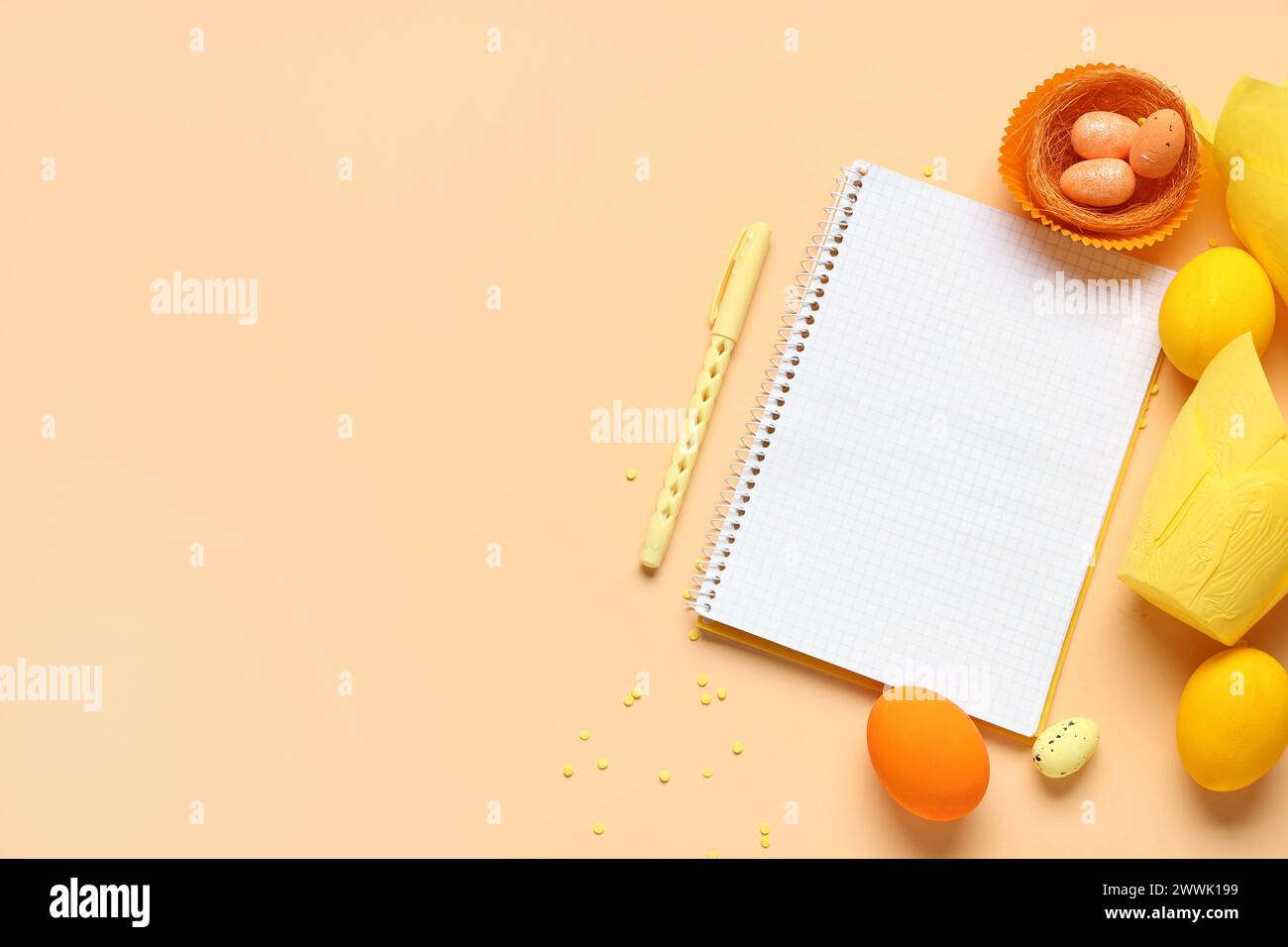 Blank notepad for recipes with pen, Easter eggs and baking molds on orange background Stock Photo