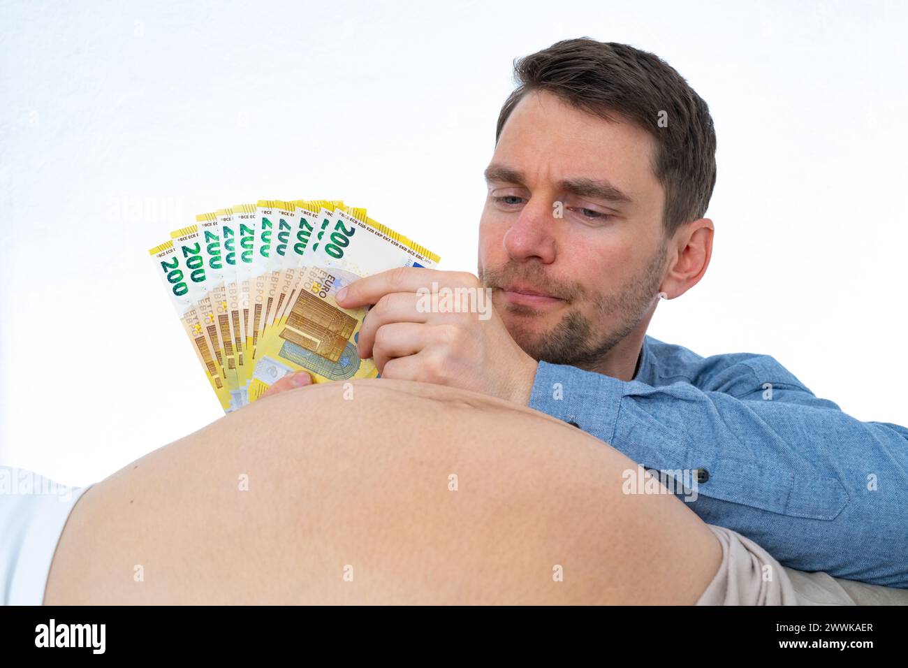 Description: Thoughtful father is mentally counting out expenses for the baby and pulling out banknotes of his hand while looking at his wife's pregna Stock Photo