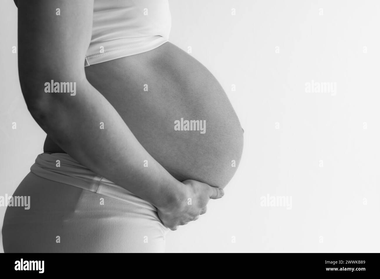 Description: Midsection of unrecognizable standing mother in white cloths with very round pregnant baby belly. Final month of pregnancy - week 36. Sid Stock Photo