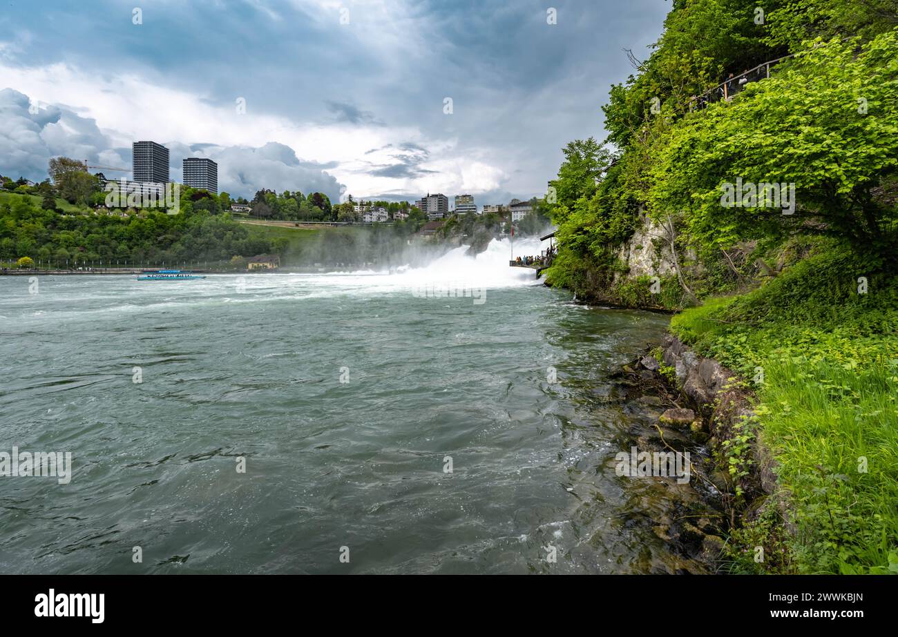 Description: Tourists enjoy the enormous water floods of the mighty Rhine Falls from the viewing platform and the toursut boat. Rhine Falls, Neuhausen Stock Photo