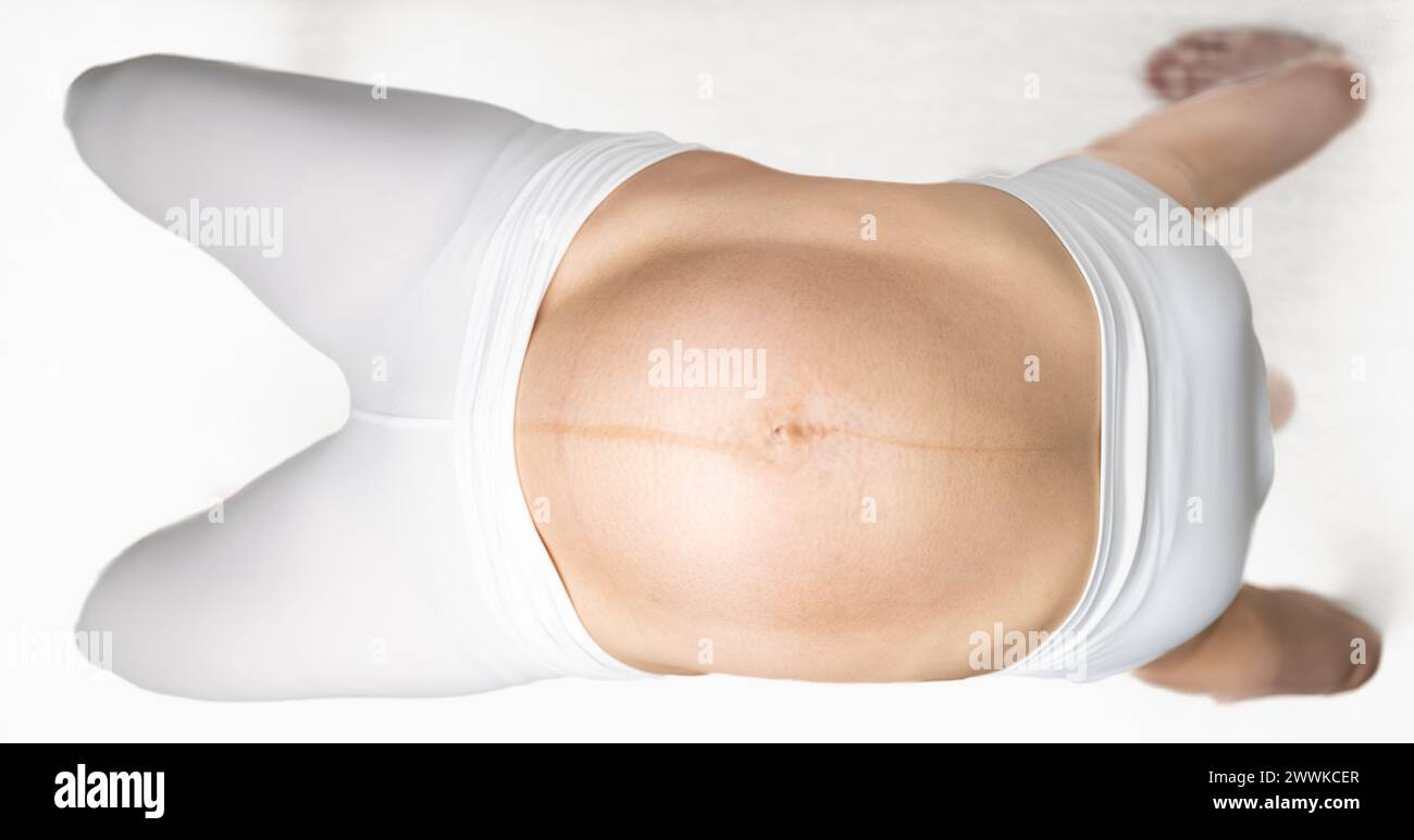Description: Sporty pregnant woman making the bridge exercise in last month of pregnancy. Third trimester - week 36. Top view. White background. Brigh Stock Photo