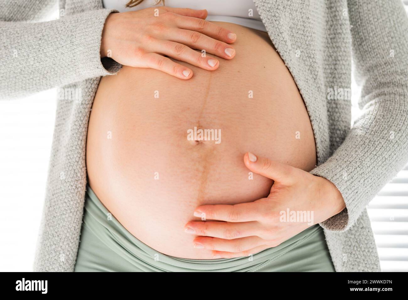 Description: Front view of midsection of unrecognizable woman gently holding her belly in final months of pregnancy. Pregnancy first trimester - week Stock Photo