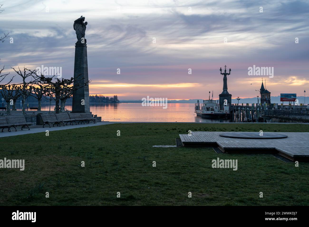 Beschreibung: Blick bei Morgendämmerung über die Hafeneinfahrt auf den See mit Imperia Statue und Grafen Zeppelin Statue im Vordergrund. Konstanz, Bod Stock Photo