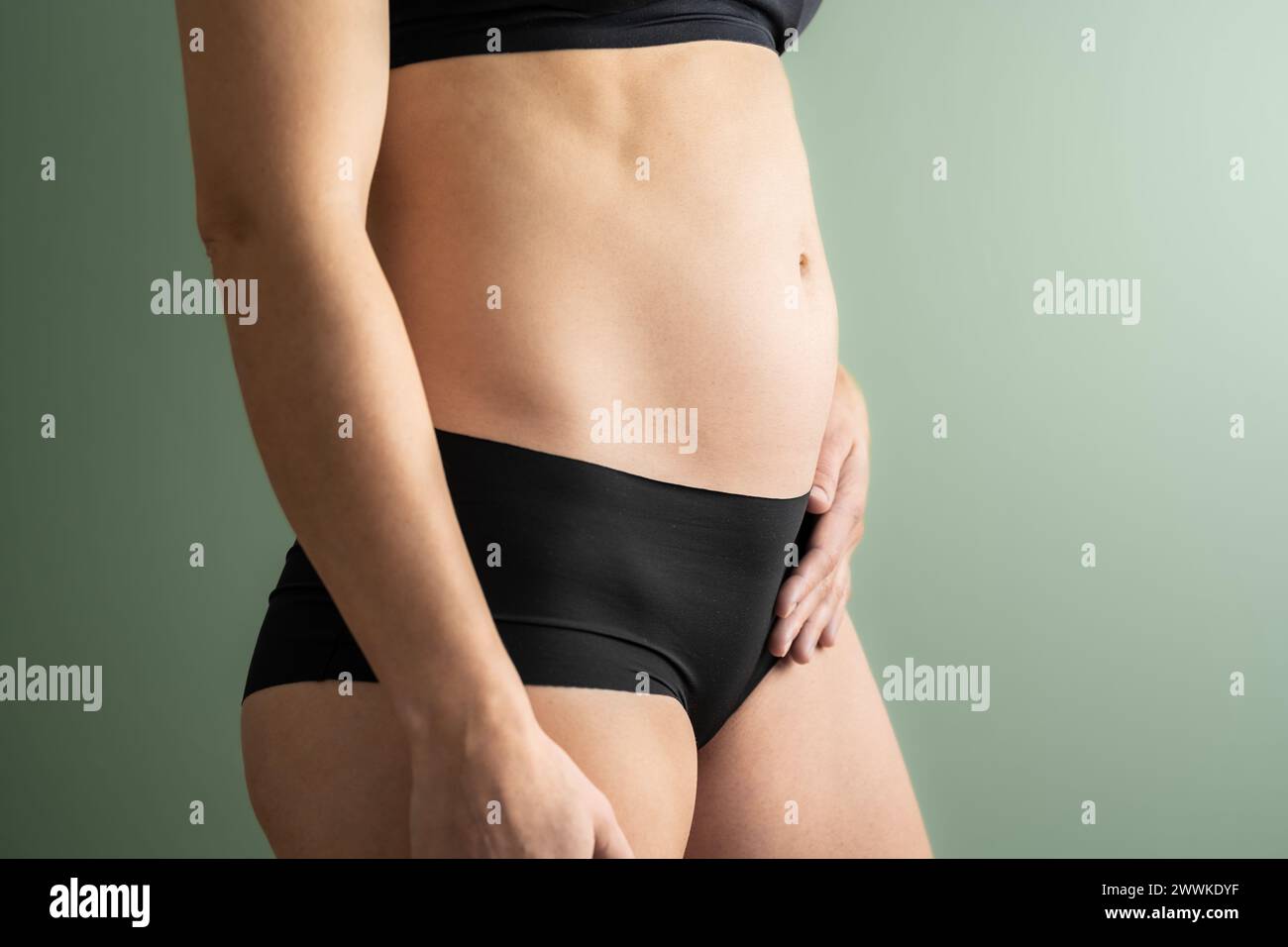 Description: Midsection view of an unrecognizable woman in the first months of pregnancy holding her belly with her left hand. Pregnancy first trimest Stock Photo