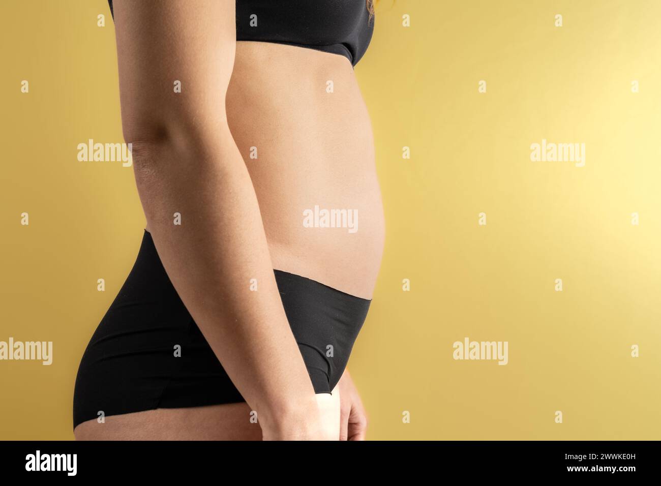 Description: Lateral midsection view of an unrecognizable woman's belly in the first months of pregnancy. Pregnancy first trimester - week 18. Side vi Stock Photo