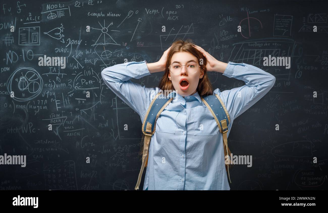 Back to school. Unhappy teenager indoors. Girl is learning in class on background of blackboard. Stock Photo