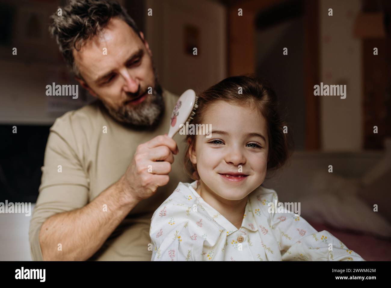 Father combing and braiding daughter's hair as part of bedtime routine. Single dad taking care of his daughter's hairstyle. Stock Photo