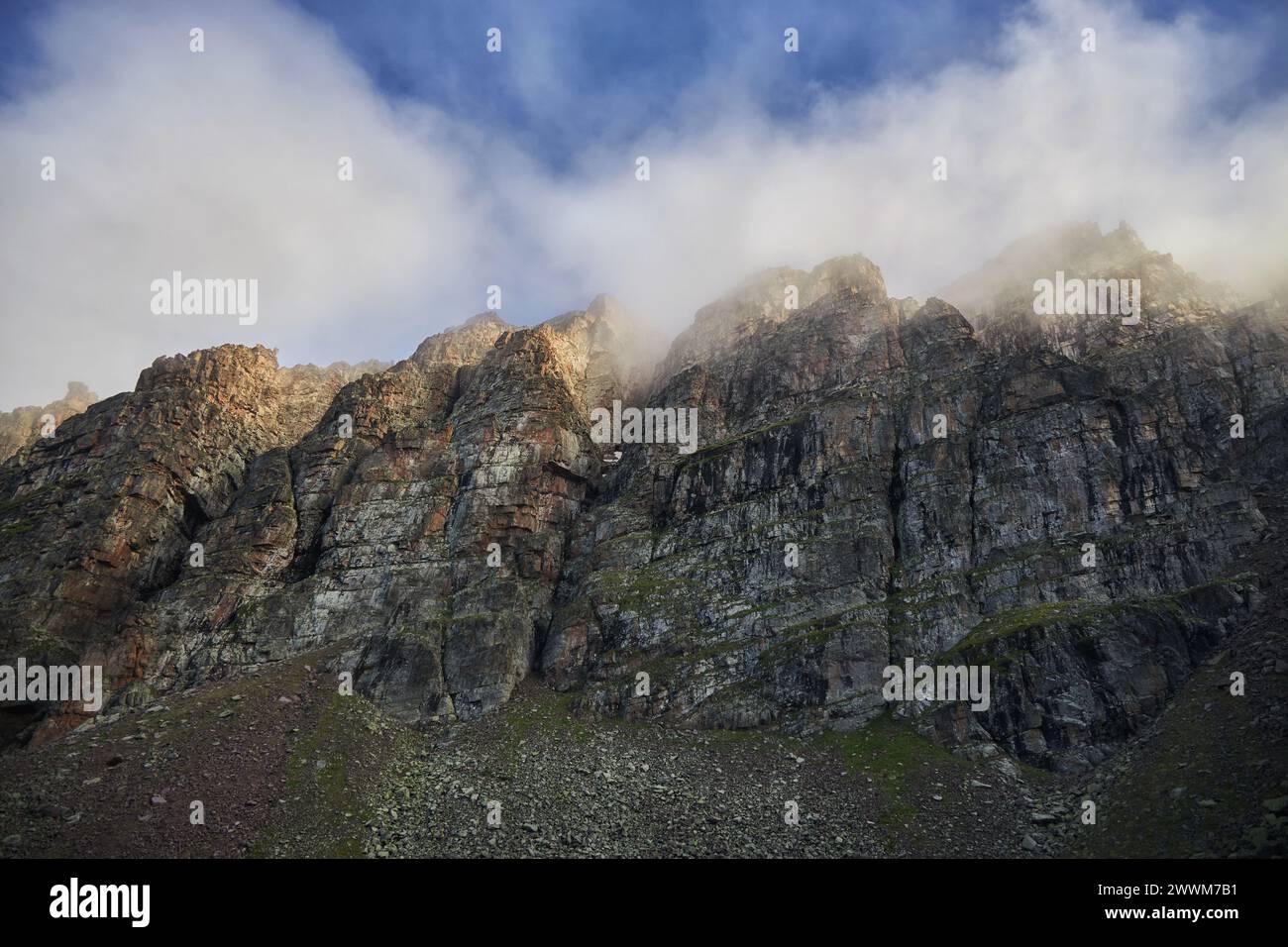 Mist wraps the rugged peaks of a mountain range, with the morning sun illuminating the scene Stock Photo