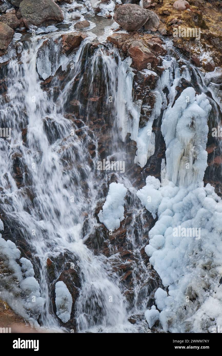 Chilly cascade waterfall, where water rushes over icy rocks, intertwining liquid flow with frozen formations Stock Photo