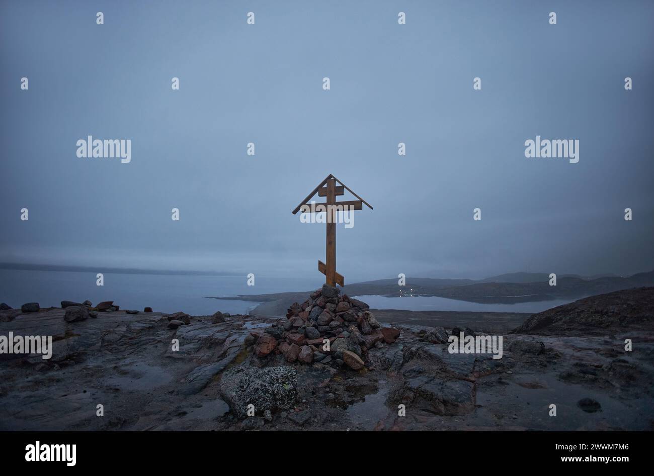 Simple wooden cross atop a rocky hill, with a foggy coastal backdrop under the evening sky Stock Photo