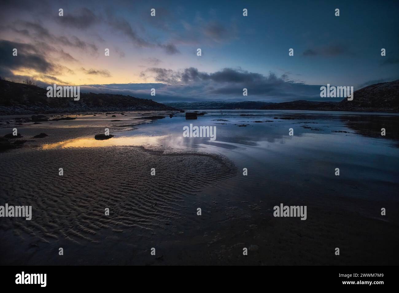 Twilight sky with clouds over a serene coastal setting, reflected in calm tidal pools Stock Photo
