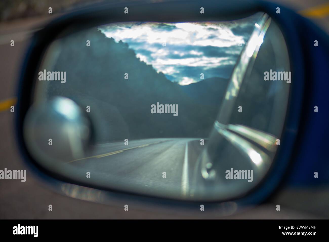 Through the rear-view window, the car captures a snapshot of the road, offering a glimpse of the journey's perspective and traffic behind. Stock Photo