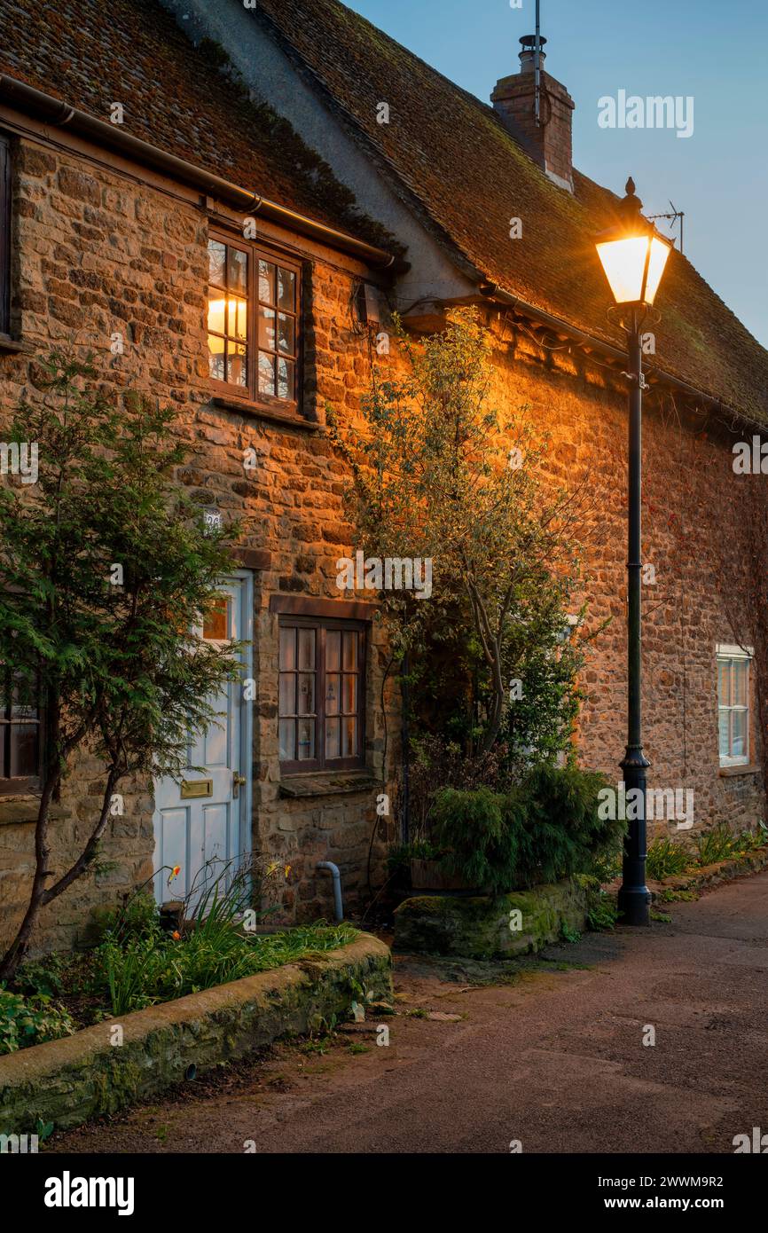 Stone cottage lit up by a street light at dusk.  Kings Sutton, Northamptonshire, England Stock Photo