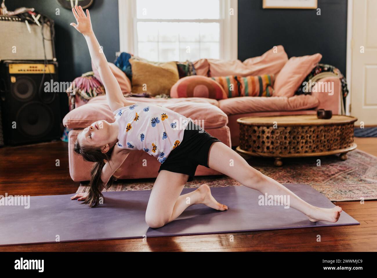 Young girl does side plank on purple yoga mat in living room Stock Photo