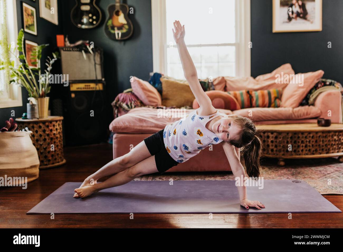 Young girl does side plank on purple yoga mat in living room Stock Photo
