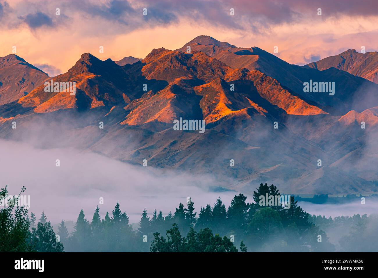 A horizontal photo of a sunrise with colorful clouds over the mountains and morning mist in the valley in Hanmer Springs, a town in the Canterbury reg Stock Photo